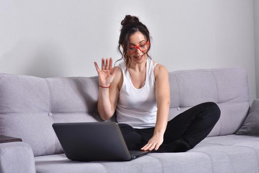 Beautiful brunette woman in red glasses on sofa using laptop