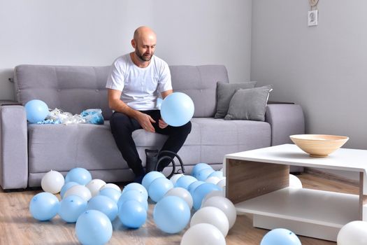 Celebration, holidays, party concept. Happy hairless man preparing to party. Blowing blue and white balloons