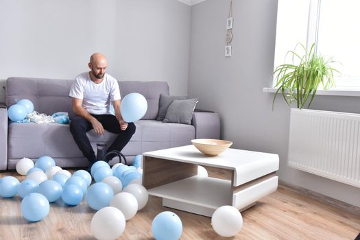 Celebration, holidays, party concept. Happy hairless man preparing to party. Blowing blue and white balloons