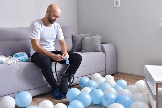 Celebration, holidays, party concept. Happy hairless man preparing to party. Blowing blue and white balloons