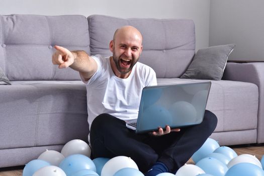 Positive young man in casual clothes sitting in livingroom and using laptop computer