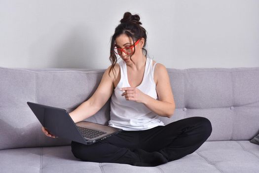 Beautiful brunette woman in red glasses on sofa using laptop