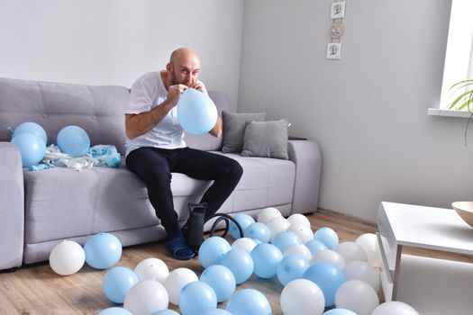 Celebration, holidays, party concept. Happy hairless man preparing to party. Blowing blue and white balloons