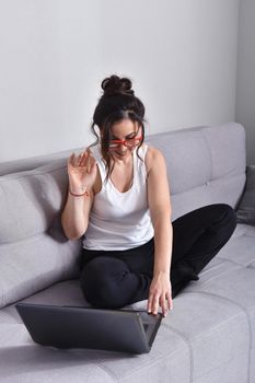 Beautiful brunette woman in red glasses on sofa using laptop