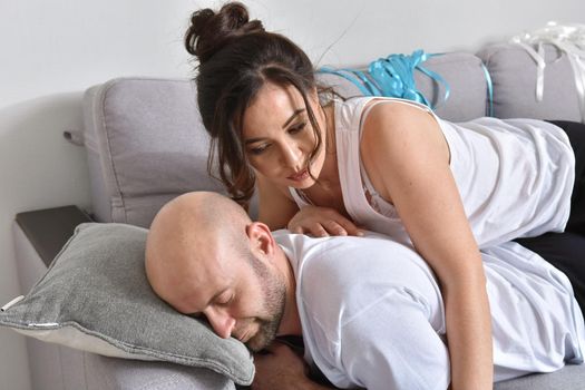 Photo of cheerful romantic caucasian family couple smiling and hugging while sitting on sofa at home. Man and woman in love