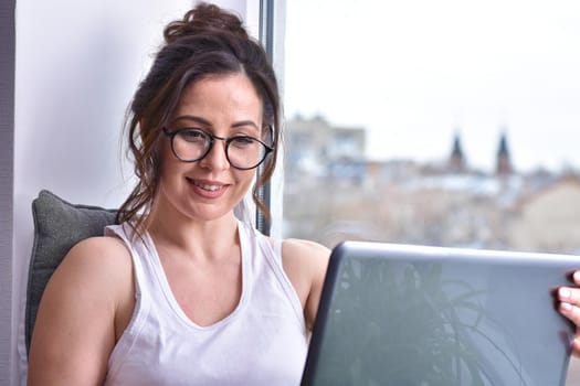 Home quarantine, protection from coronavirus. Caucasian brunette woman sit on window with computer