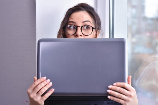 Home quarantine, protection from coronavirus. Caucasian brunette woman sit on window with computer