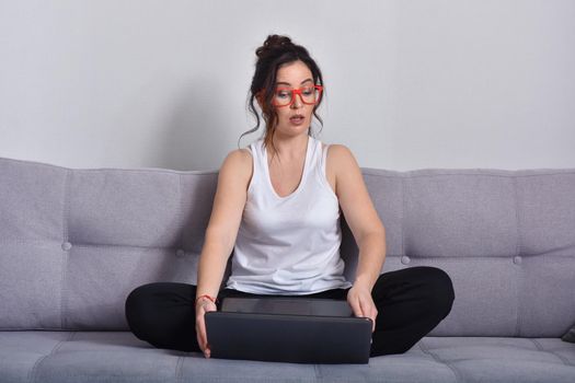 Beautiful brunette woman in red glasses on sofa using laptop