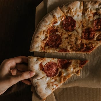 A large round juicy mouth-watering pizza with cheese and salami lies on a cardboard box from a delivery package. paper backing. close view. see flour. good thin dough