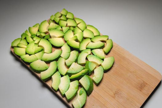 Avocado slices on a wooden board, on a gray table top view