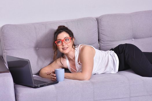 Beautiful brunette woman in red glasses on sofa using laptop