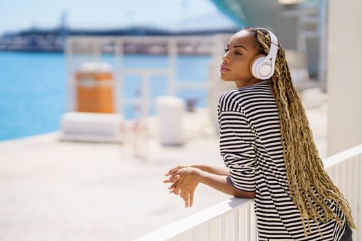 Beautiful young black woman listening to music while enjoying the view of the seaport.