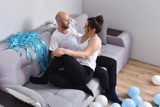 Photo of cheerful romantic caucasian family couple smiling and hugging while sitting on sofa at home. Man and woman in love