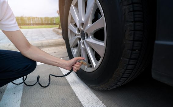 Woman inflates the tire. Woman checking tire pressure and pumping air into the tire of car wheel. Car maintenance service for safety before travel. Tire inflating point. Filling air in the tyre of car