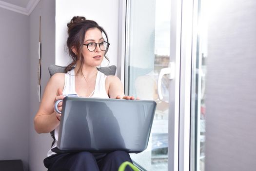 Home quarantine, protection from coronavirus. Caucasian brunette woman sit on window with computer