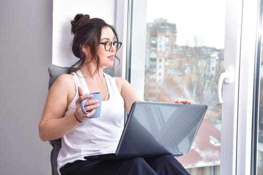 Home quarantine, protection from coronavirus. Caucasian brunette woman sit on window with computer