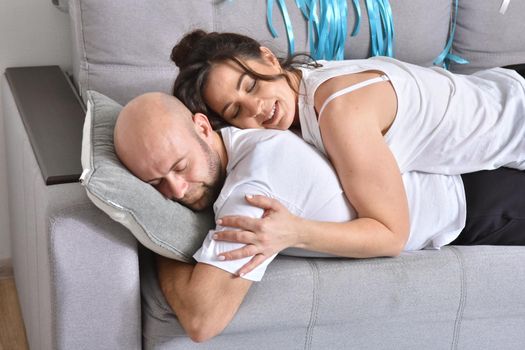 Photo of cheerful romantic caucasian family couple smiling and hugging while sitting on sofa at home. Man and woman in love