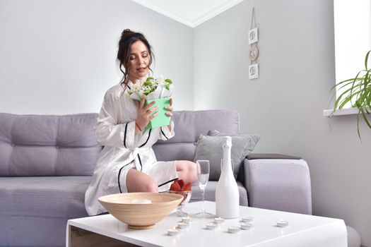 Beautiful brunette woman dressing gown with bouquet indoors. Female portrait in living room