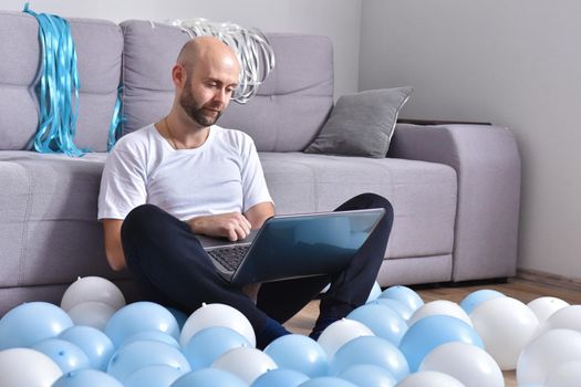 Positive young man in casual clothes sitting in livingroom and using laptop computer