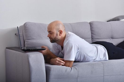 Positive young man in casual clothes sitting in livingroom and using laptop computer