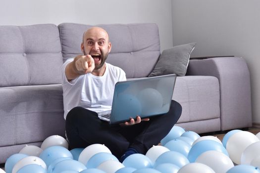 Positive young man in casual clothes sitting in livingroom and using laptop computer