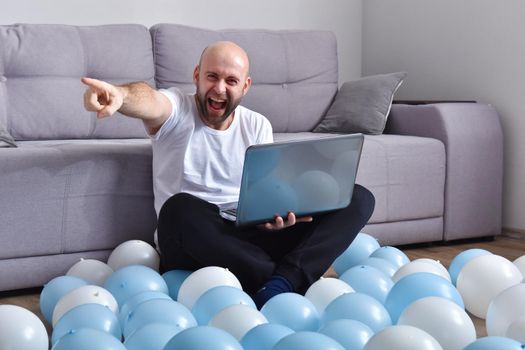 Positive young man in casual clothes sitting in livingroom and using laptop computer