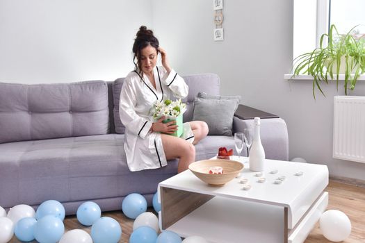 Beautiful brunette woman dressing gown with bouquet indoors. Female portrait in living room