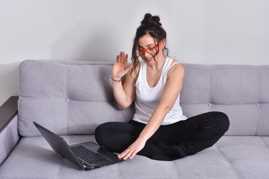 Beautiful brunette woman in red glasses on sofa using laptop