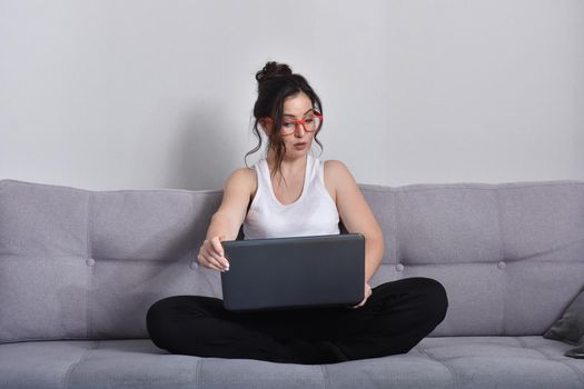 Beautiful brunette woman in red glasses on sofa using laptop