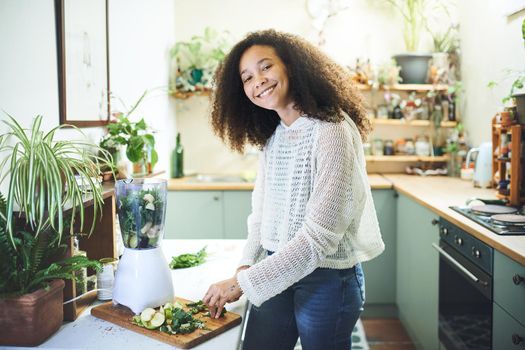 Beautiful african woman smiling at the camera while making a smoothie for breakfast. High quality photo