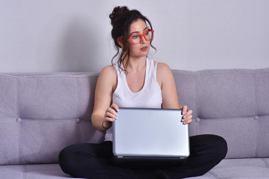 Beautiful brunette woman in red glasses on sofa using laptop