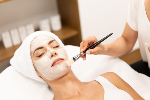 Aesthetics applying a mask to the face of a Middle-aged woman in modern wellness center. Beauty and Aesthetic concepts.