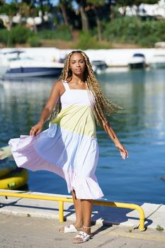Young black woman walking along a seaport wearing a nice summer dress.