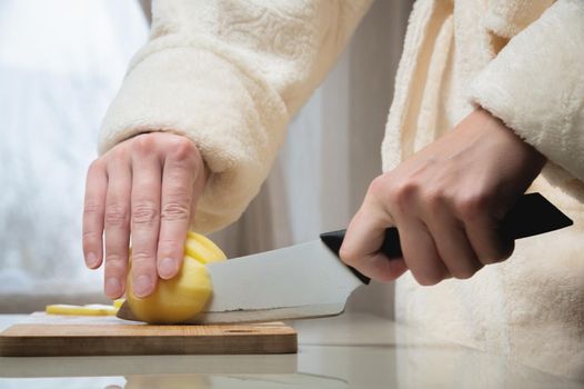 Close-up of female hands cutting peeled potatoes on a wooden cutting board. Home cooking potatoes.