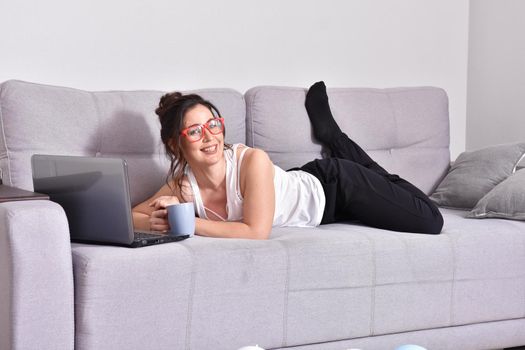 Beautiful brunette woman in red glasses on sofa using laptop