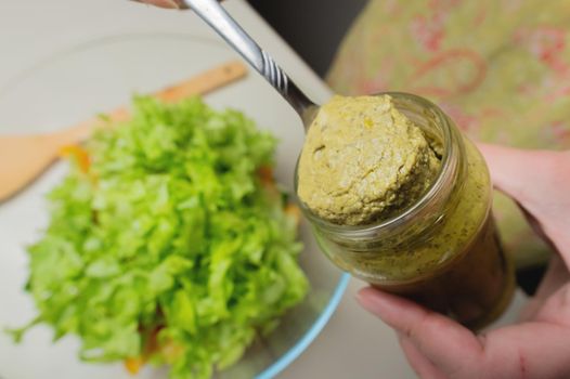 woman's hand with a jar in the kitchen, from which salad sauce is taken out with a spoon. top view close-up