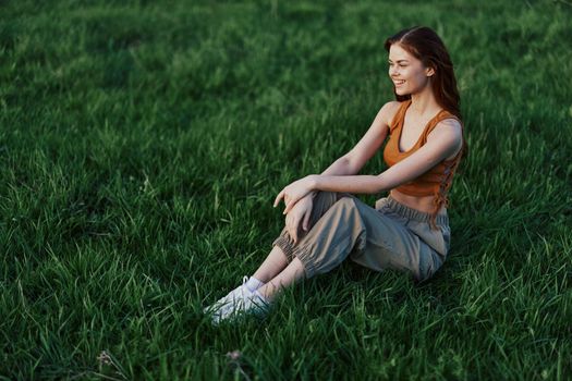 A happy woman looks out at the setting summer sun sitting on the fresh green grass in the park and smiling, view from above. The concept of self-care. High quality photo
