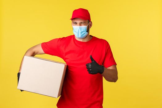 Express delivery during pandemic, covid-19, safe shipping, online shopping concept. Reliable transfer company, courier in red uniform and medical mask, provide contactless deliver, holding box parcel.
