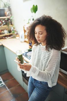 Young african girl browsing on social media while enjoying her green smoothie