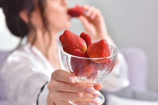 Portrait of happy young brunette woman holding bowl of juicy red strawberries