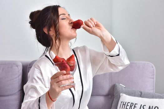 Portrait of happy young brunette woman holding bowl of juicy red strawberries