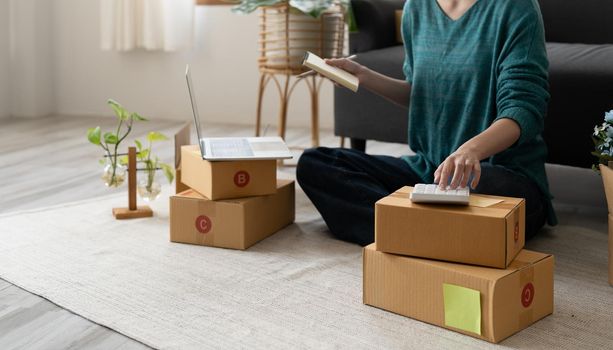 Entrepreneur using calculator with pencil in her hand, calculating financial expense at home office,online market packing box delivery,Startup successful small business owner, SME, concept.