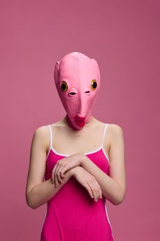 Woman standing in a pink fish mask on her head, a provocative crazy Halloween look, pink background in the studio . High quality photo