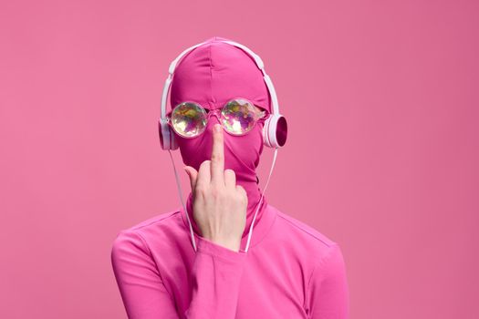 Conceptual creative art photo of a man in Total Pink on a pink background wearing a mask and glasses, who is adjusting his glasses with the middle finger of his hand. High quality photo