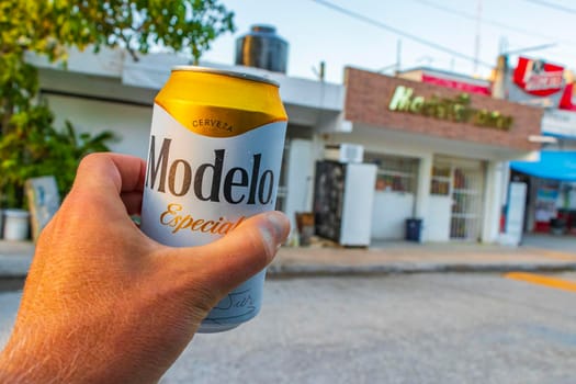 Chemuyil Mexico 02. February 2022 Modelo beer can in the hand with cityscape landscape and store of Chemuyil in Quintana Roo Mexico.