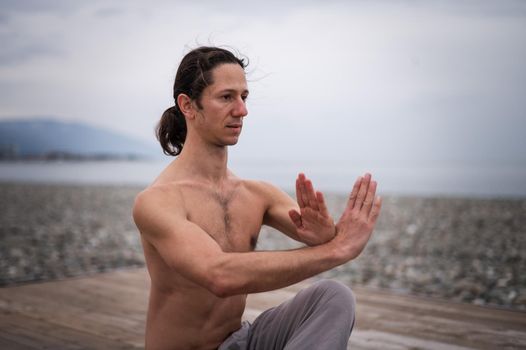 Caucasian man with naked torso practicing wushu on the seashore