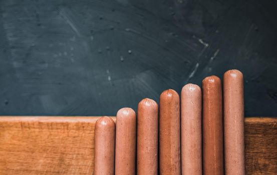 Boiled fried sausages sausages lie on a wooden kitchen board scratched against a dark concrete background.