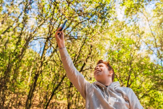 young woman taking a selfie with her mobile phone, on her summer holidays. young woman on a trip. woman walking in nature. background of a lush forest, with green plants illuminated by sun rays.