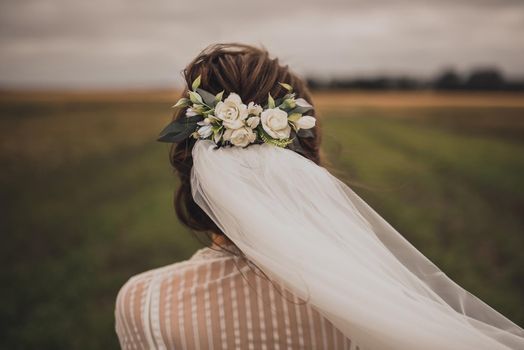 Wedding decorations jewelry on head. Beautiful green wreath with flower holds a veil. young slim beautiful woman high Greek hairstyle in White Silk in a bathrobe. green natural background