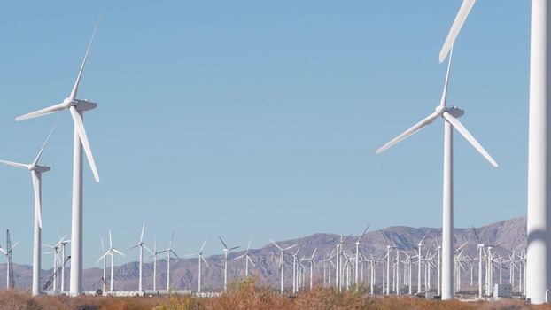 Windmills turbine rotating, wind farm power plant, alternative green renewable energy generators, industrial field in California desert USA. Electricity generation on windfarm. Palm Springs, Coachella